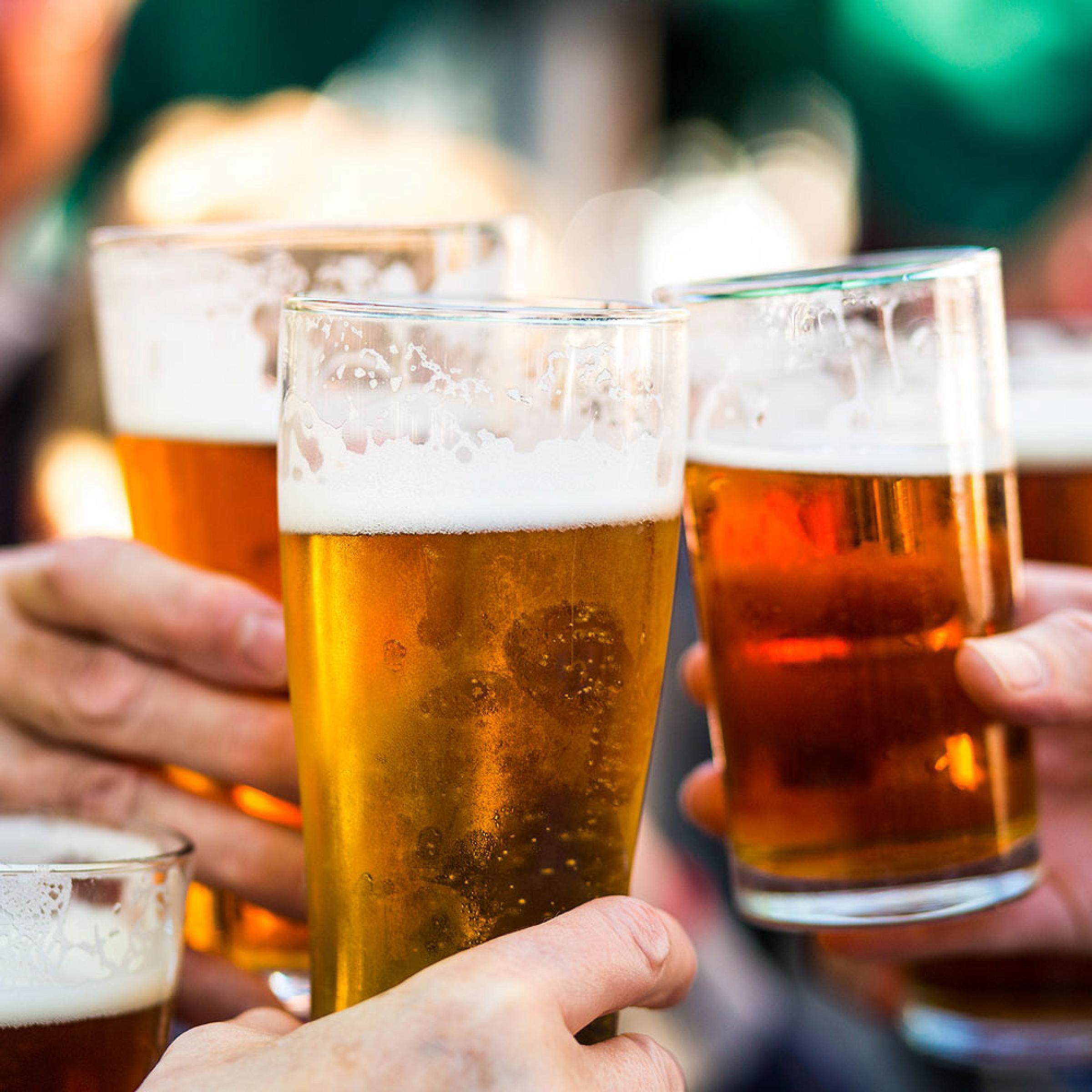 Three hands holding beer clink their glasses together.
